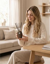 Frau sittzt auf einem Stuhl und hält die Duftvase, den Raumduft Reed Diffuser Lamia in der hand 