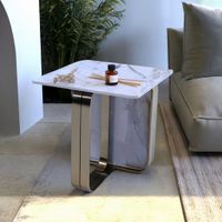 Dolce side table with champagne gold brushed stainless steel base and white premium stone top, styled in a modern living room with a beige sofa, neutral rug, indoor plant, and contemporary décor