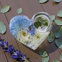 a heart shaped tea light holder created from resin containg real preserved flowers which are blue and white in colour. Resting on a wood effect background with a sprinkle of leaves