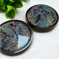 a pair of round coasters, black in colour with a blue peacock style design, resting on a white background