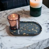 an oval trinket tray, green in colour with a gold fleck design, there is a candle resting on top. Set in a cosy home