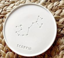 a white round coaster with star sign and constellation design resting on a hessian background