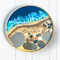 Ocean Art Design round table top created from resin, pebbles, sand and ashes, resting on a white boarded background