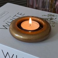 a round tea light holder with brass effect design, resting on a white book with a lit candle inside