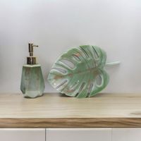 A green and gold design reed diffuser with a decorative monstera leaf resting on a wooden table top