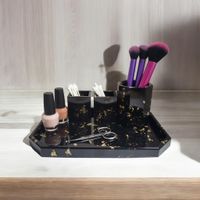 black resin vanity tray with 2 matching pots created in a black design with gold fleck, resting on a light sideboard