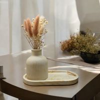 a decorative pot resting on a matching oval trinket tray, artificial flowers inside. The background is a cosy home
