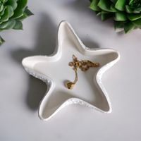 White dish shaped like a star fish, there is a necklace resting inside, set on a white background