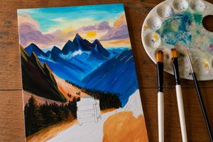 Werk in uitvoering van een handgeschilderd berglandschap met camper, naast verfkwasten en schilderspalet van Studio Lof.